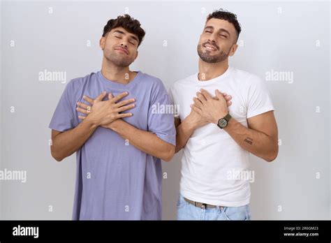Homosexual Gay Couple Standing Over White Background Smiling With Hands On Chest With Closed