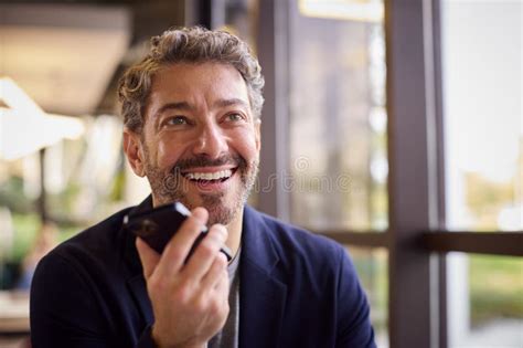 Mature Businessman Working At Desk In Office Talking Into Mic Of Mobile Phone Stock Image