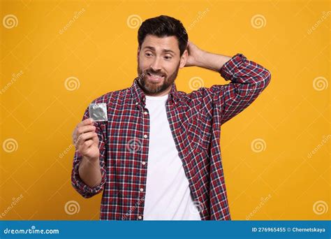Confused Man Holding Condom On Yellow Background Safe Sex Stock Image Image Of Package