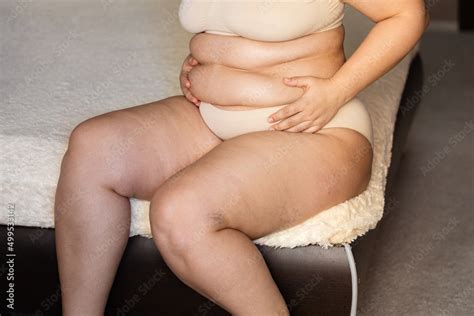 Unrecognizable Fat Plus Size Overweight Woman Sitting On Edge Of Beige Plaid In Nude Bra