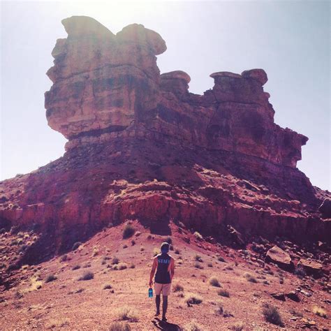 A Man Standing On Top Of A Dirt Field Next To A Tall Rock Formation In