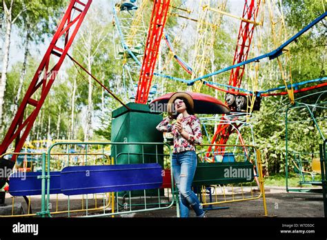 Portrait Of Brunette Girl In Pink Glasses And Hat With Ice Cream At Amusement Park Stock Photo