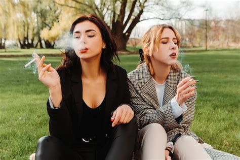 Premium Photo Two Pretty Women Friends Sitting On Grass Smoking Cigarette Couple Of Gay