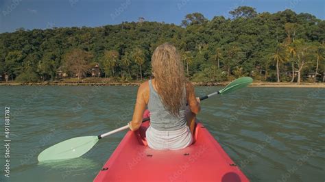 Long Haired Blonde Woman With Sunglasses Rows Bright Pink Canoe Along Sea Bay Water To Beach