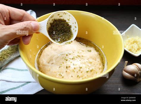 Hand Pouring Olive Oil With Herbs Onto Kneaded Dough For Baking Italian