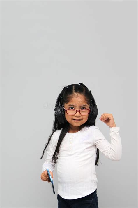 4 Year Old Brunette Latin Girl With Glasses Listens To Music In Her Headphones Connected To Her