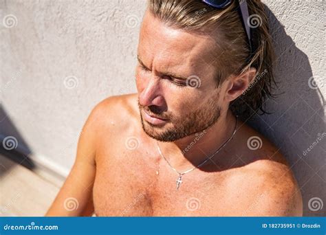 The Handsome Brutal Man In Sunglasses With A Long Hair And Naked Torso Sits Near The Pool Eyes