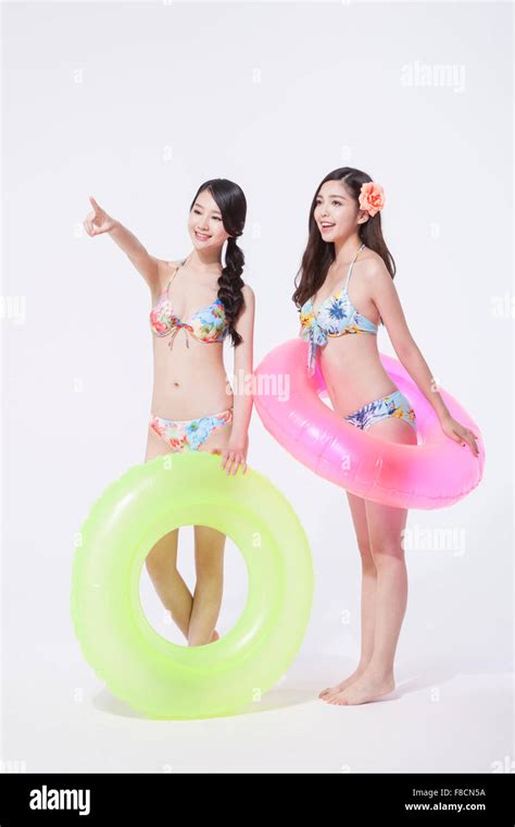 Two Women In Bikini Holding A Ring Tube Each And Standing And A Woman Pointing With Her Finger