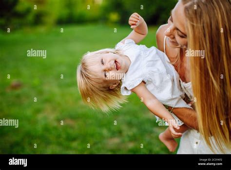 Schlanke blonde Frau spielt mit ihrer kleinen Tochter im Sommerpark Mädchen tragen weiße