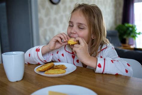 A Pretty Blonde Baby In Cute Pajamas Is Sitting At A Comfortable Table In The Kitchen And