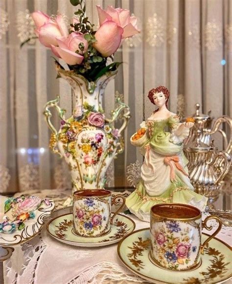 A Table Topped With Tea Cups And Saucers Filled With Flowers Next To A Vase