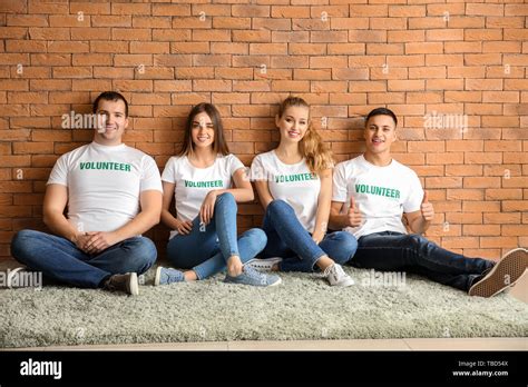 Team Of Young Volunteers Sitting Near Brick Wall Stock Photo Alamy