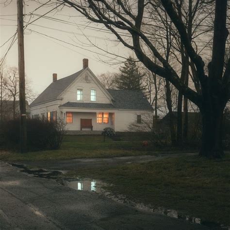 A White House Sitting On The Side Of A Road Next To Some Trees And Grass