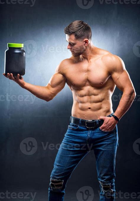 Male Athlete Bodybuilder With A Naked Torso Stands With A Jar Of Sports Nutritional Supplements