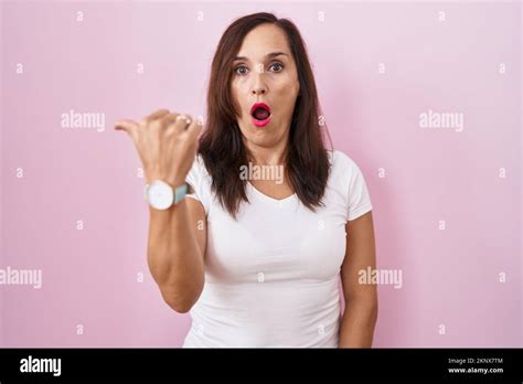 Middle Age Brunette Woman Standing Over Pink Background Surprised Pointing With Hand Finger To