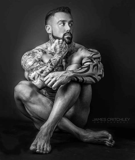 A Man With Tattoos Sitting On The Ground In Front Of A Black And White