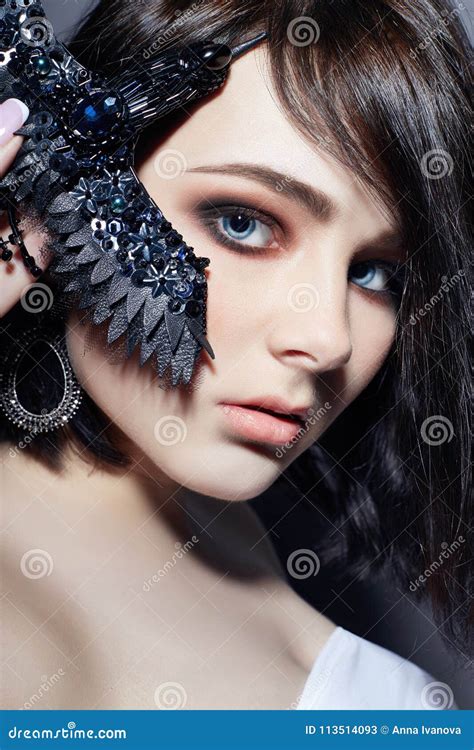 Όμορφο κορίτσι Brunette με τα μεγάλα μπλε μάτια που κρατούν μια μαύρη διακόσμηση πορπών υπό