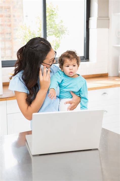 Smiling Brunette Holding Her Baby And Using Laptop On Phone Call Stock Photo Image Of Girl