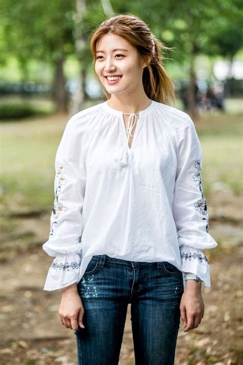 A Woman Standing In The Park Wearing Jeans And A White Top With Embroidered Details On It