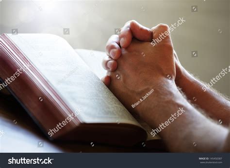 Hands Folded In Prayer On A Holy Bible In Church Concept For Faith