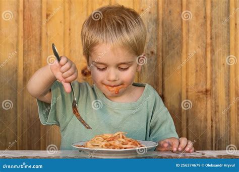 A Little Boy Is Eating Spaghetti His Face Is Smeared With Ketchup