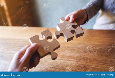 Two People Holding And Putting A Piece Of Wooden Jigsaw Puzzle Together