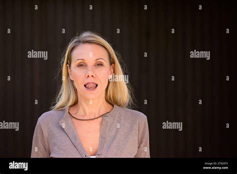 Portrait Of An Attractive Blonde Woman Sticking Out Her Tongue In Front Of Wooden Wall Stock