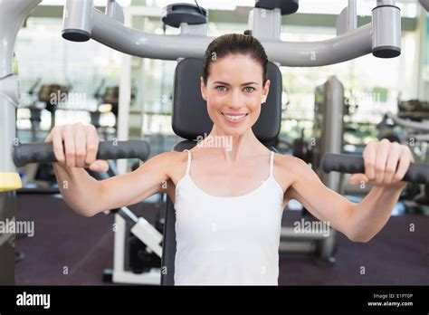 Fit Brunette Smiling At Camera Using Weights Machine For Arms Stock Photo Alamy