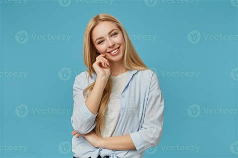 Positive Blonde Long Haired Lady In Blue Shirt And Grey T Shirt Casual Clothes Posing Over Blue