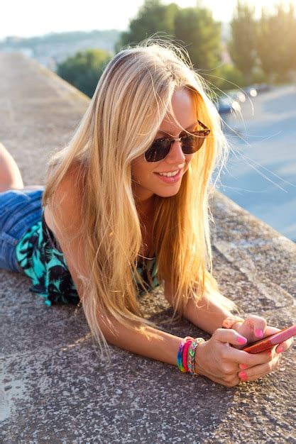 Belle fille blonde assise sur le toit avec un téléphone portable Photo Gratuite