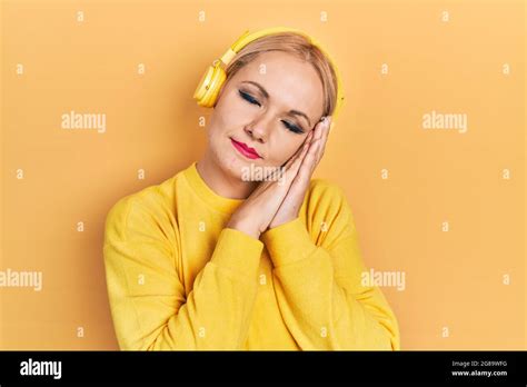 Jeune femme blonde qui écoute de la musique à l aide d écouteurs dormant fatigué rêvant et