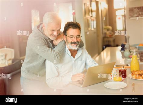 Male Gay Couple Using Laptop At Breakfast Kitchen Counter Stock Photo Alamy