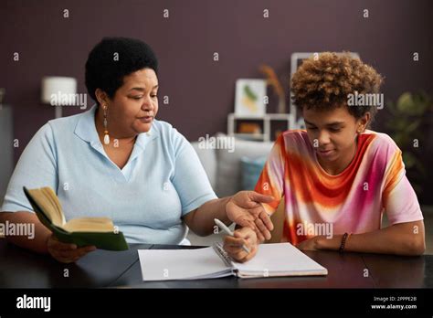 Confident Mature Female Tutor Pointing At Notes In Copybook And Explaining Something To Teenage