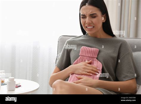 Woman Using Hot Water Bottle To Relieve Abdominal Pain On Sofa At Home Stock Photo Alamy