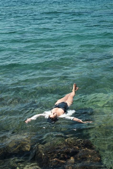 Woman In Black Bikini And White Shirt Lying On Transparent Turquoise Water Surface Vertical