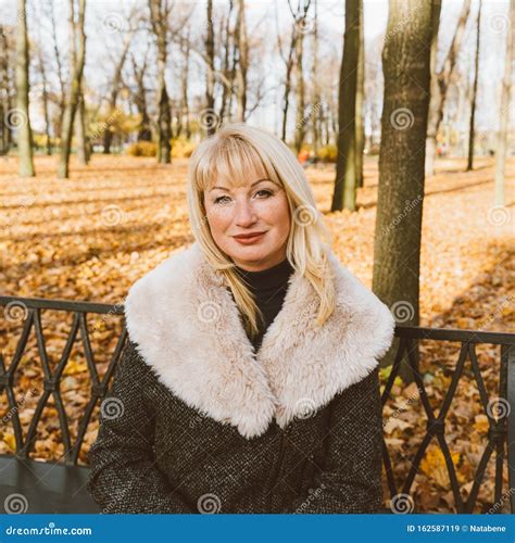 Une Heureuse Femme Blonde Mature Est Assise Sur Un Banc Dans Le Parc D Automne Et R Fl Chit Une