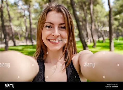 Cute Brunette Woman Wearing Sports Bra Standing On City Park Outdoors Taking Selfie On Front