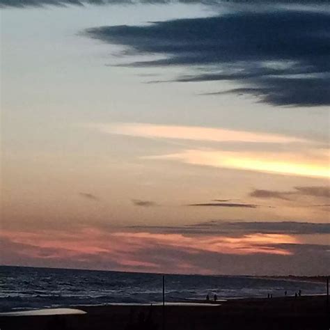 The Sun Is Setting Over The Ocean And People Are Walking On The Beach