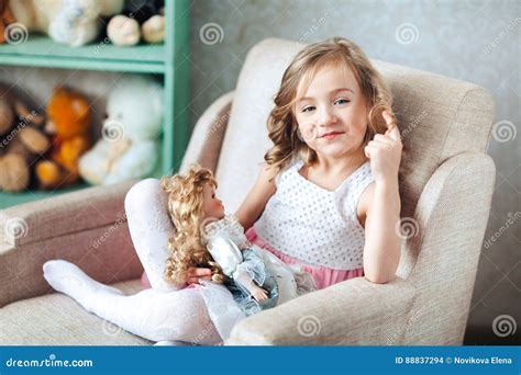Het Leuke Blonde Meisje In Witte Kleding Zit In Stoel En Glimlachen Het Haar Van Vingerdraaien