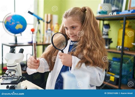 Adorable Blonde Girl Student Looking Sample With Loupe At Laboratory Classroom Stock Photo