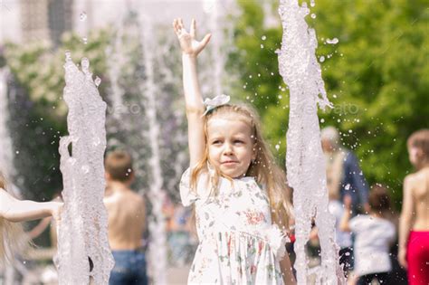 A Cute Girl With Blonde Hair Is Playing With Splashes Of Water And Raised Her Hand Up Stock