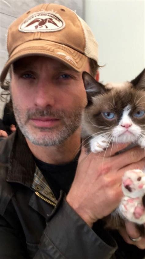 A Man Holding A Cat In His Right Hand And Wearing A Hat On Top Of Him