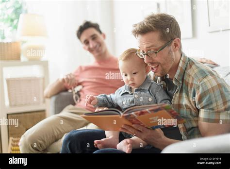Caucasian Gay Fathers Reading To Baby In Living Room Stock Photo Alamy