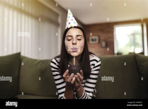 Birthday Girl Brunette In Cardboard Hat Sits On The Couch Or Sofa And Blows Out Burning Candle