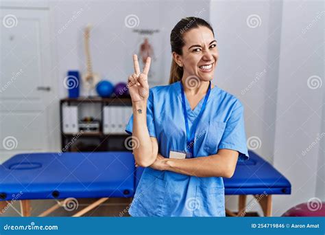 Young Hispanic Woman Wearing Physiotherapist Uniform Standing At Clinic Smiling With Happy Face