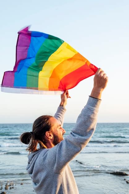 Silhueta de um homem segurando uma bandeira de arco íris do orgulho gay ao vento em uma praia