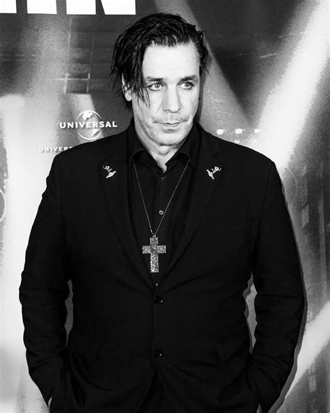 A Man In A Black Suit And Cross Necklace