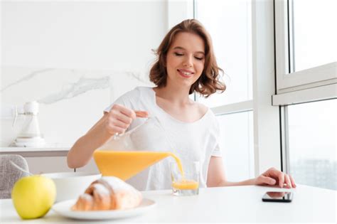 Free Cheerful Brunette Woman Pouring Juice Into Glass While Sitting