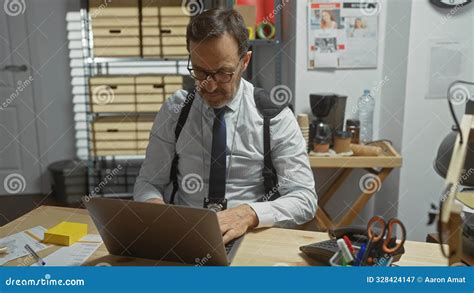 Mature Man With Glasses And Suspenders Intently Working On Laptop In An Organized Office Setting