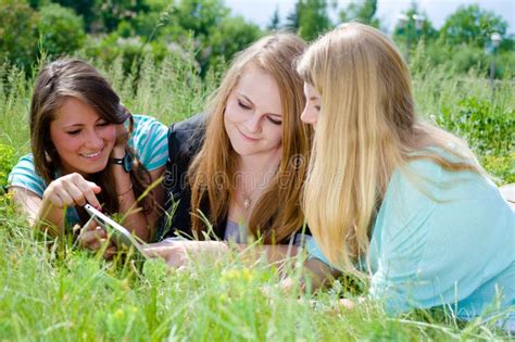 Trois Jeunes Filles De Blonde Et De Brune à L aide Du Comprimé Photo stock Image du regarder